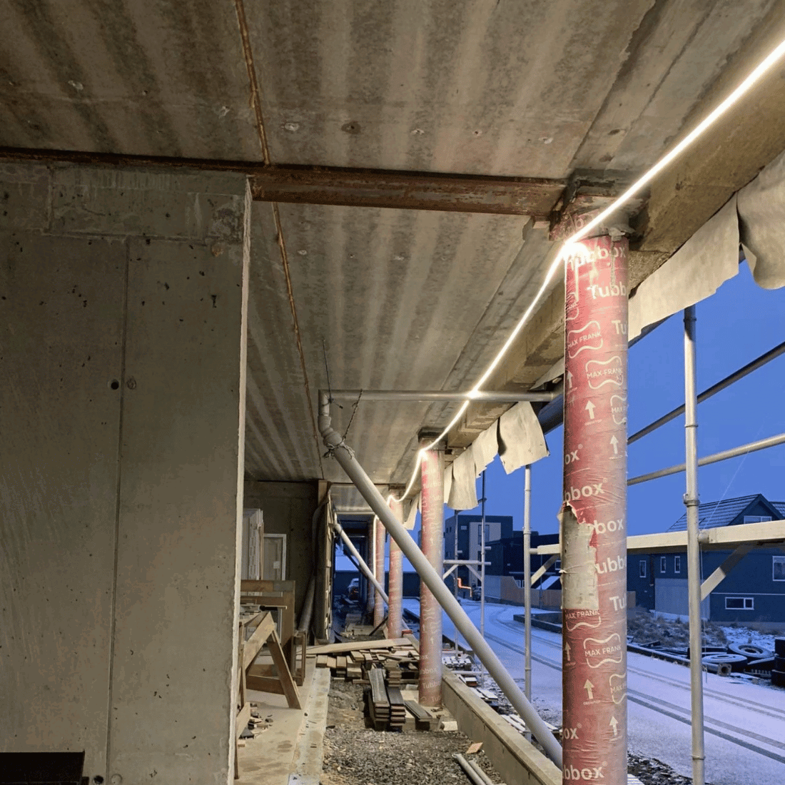 Monterad LED-strip installerad under betongtak på byggarbetsplats, ger stark arbetsbelysning.