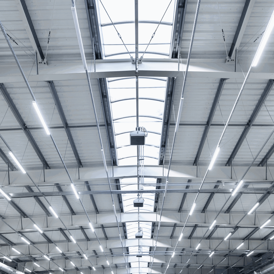 Tak i en stor lagerhall upplyst av flera 120 cm LED armaturer med neutralvit 4000K belysning. Armaturerna ger stark och jämn belysning för industriell miljö.