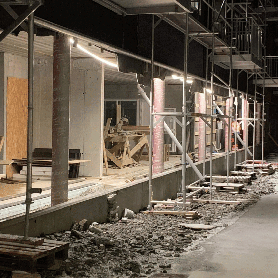 Flera LED-strips monterade längs en byggnad under konstruktion, som lyser upp arbetsområdet starkt.